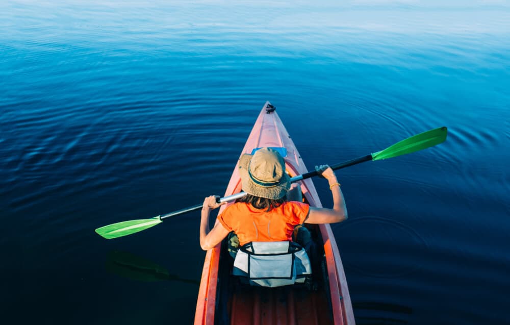 A person paddles a kayak through calm blue waters.