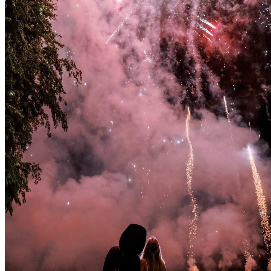 A couple watches a colorful fireworks display against a smoky night sky.