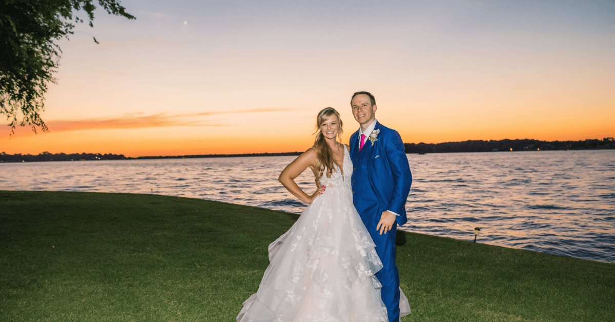 A couple poses together by a lake at sunset, celebrating their wedding. A couple poses together by a lake at sunset, celebrating their wedding.