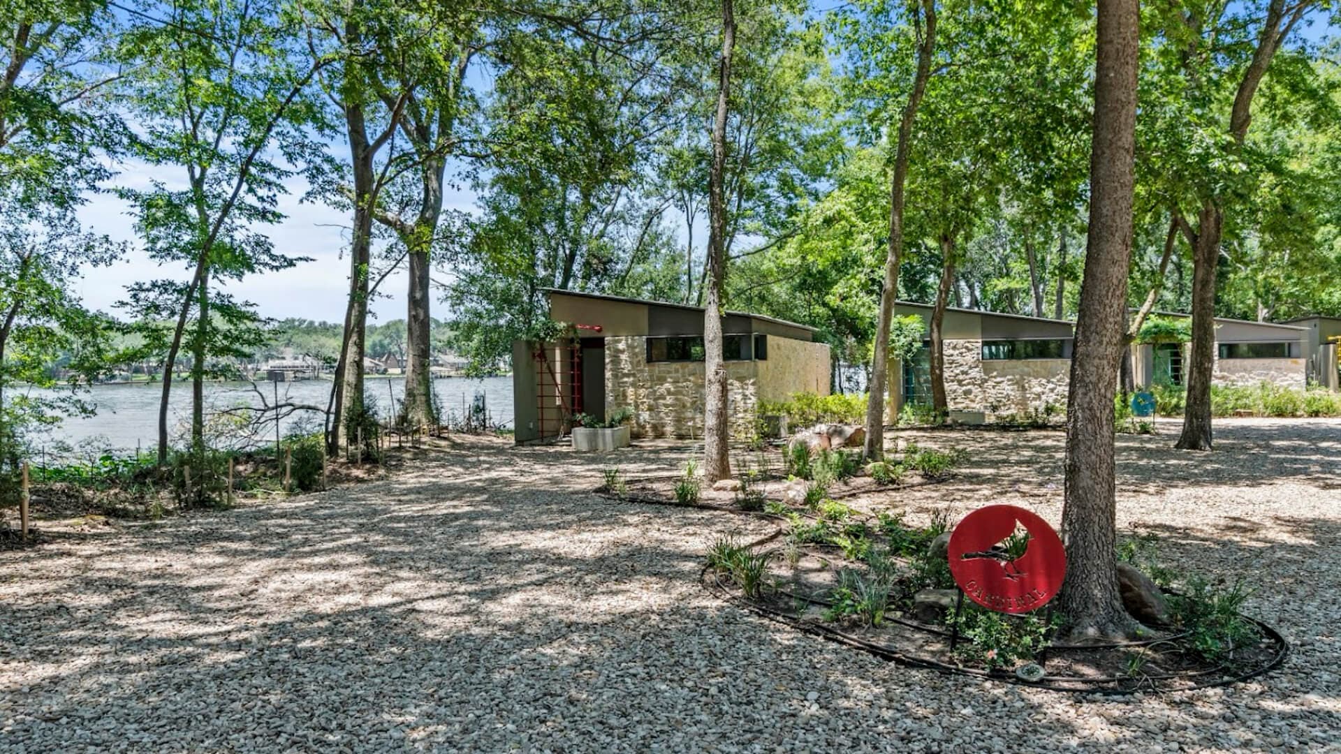 A modern building surrounded by trees and pebbled pathways near a calm waterway.