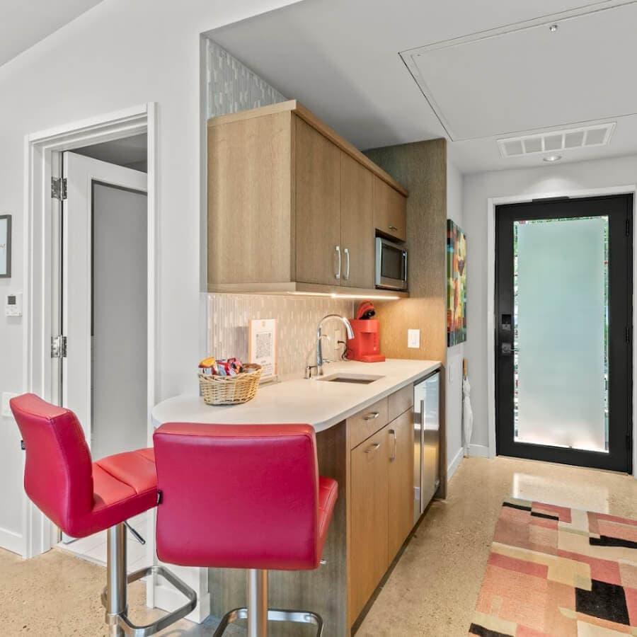 Modern kitchen featuring wooden cabinets, a red kettle, and pink bar stools.