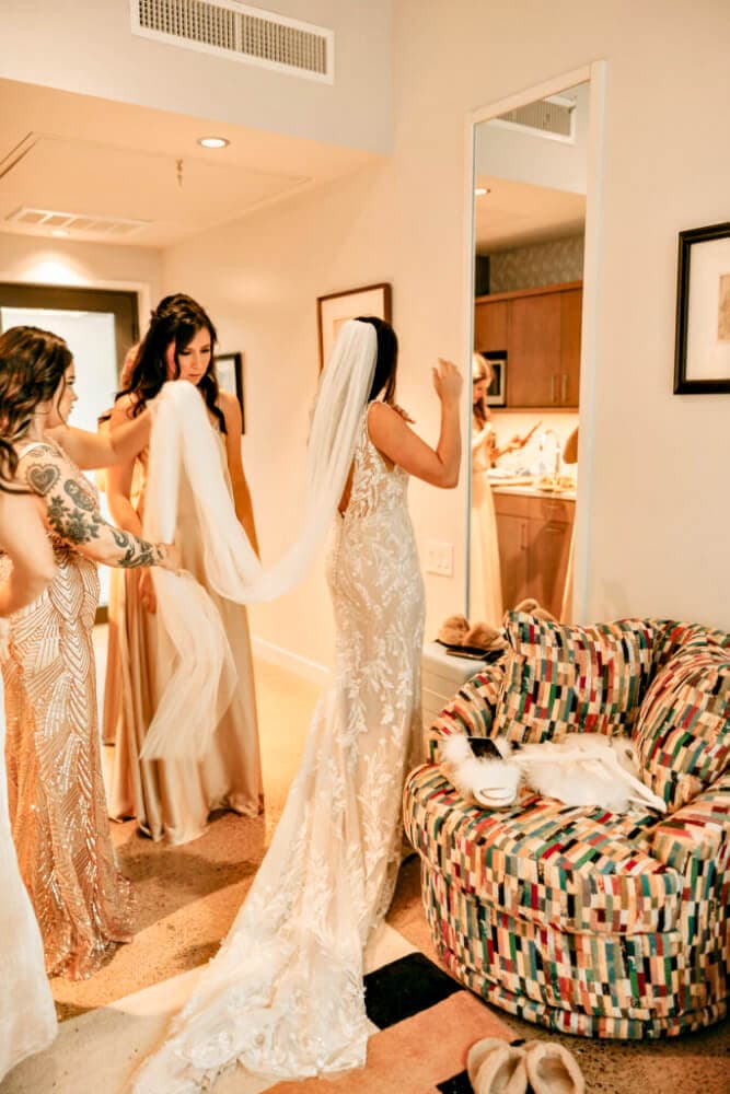 A bride adjusts her veil with the help of friends in a stylish room.
