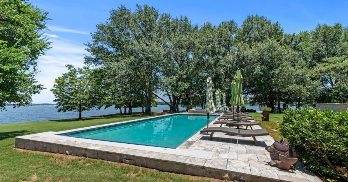 A serene swimming pool surrounded by greenery and umbrellas, overlooking a lake. A serene swimming pool surrounded by greenery and umbrellas, overlooking a lake.
