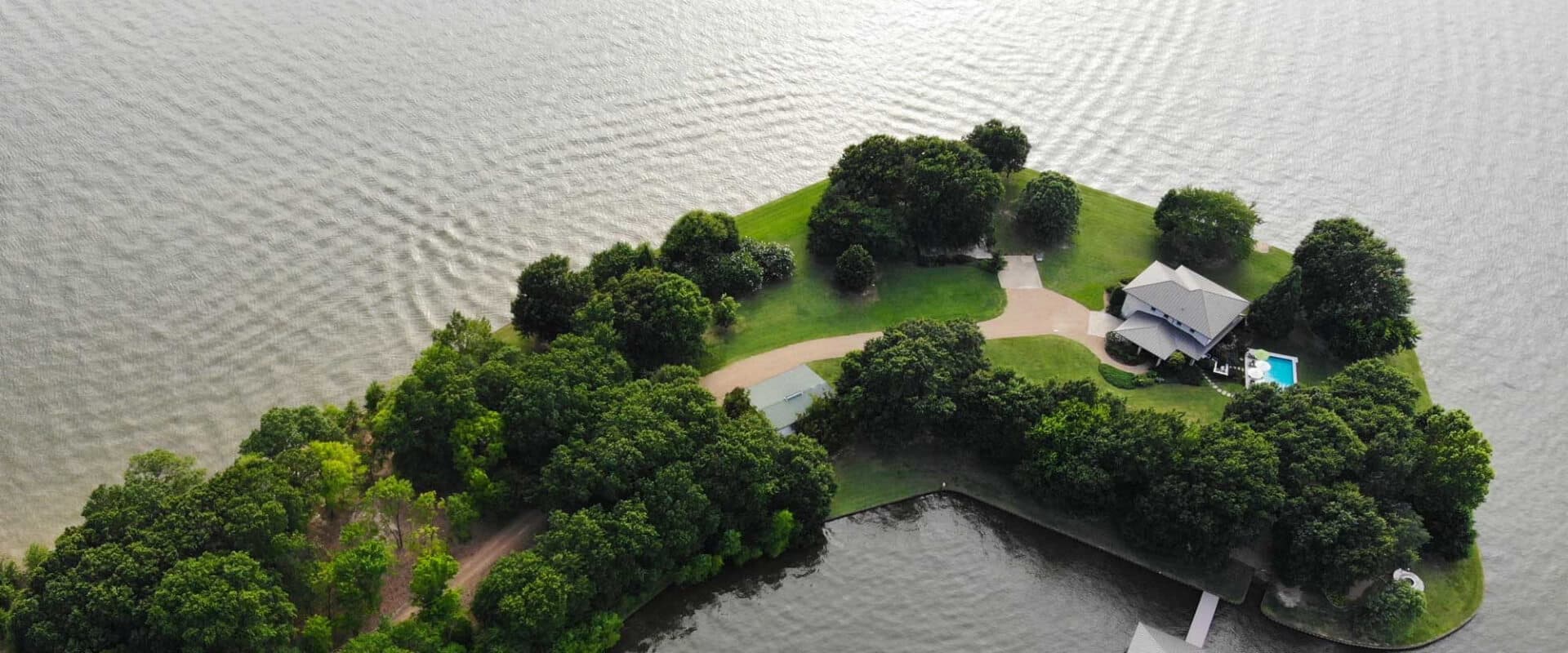 Aerial view of a lush, green island with a house and pool surrounded by water.