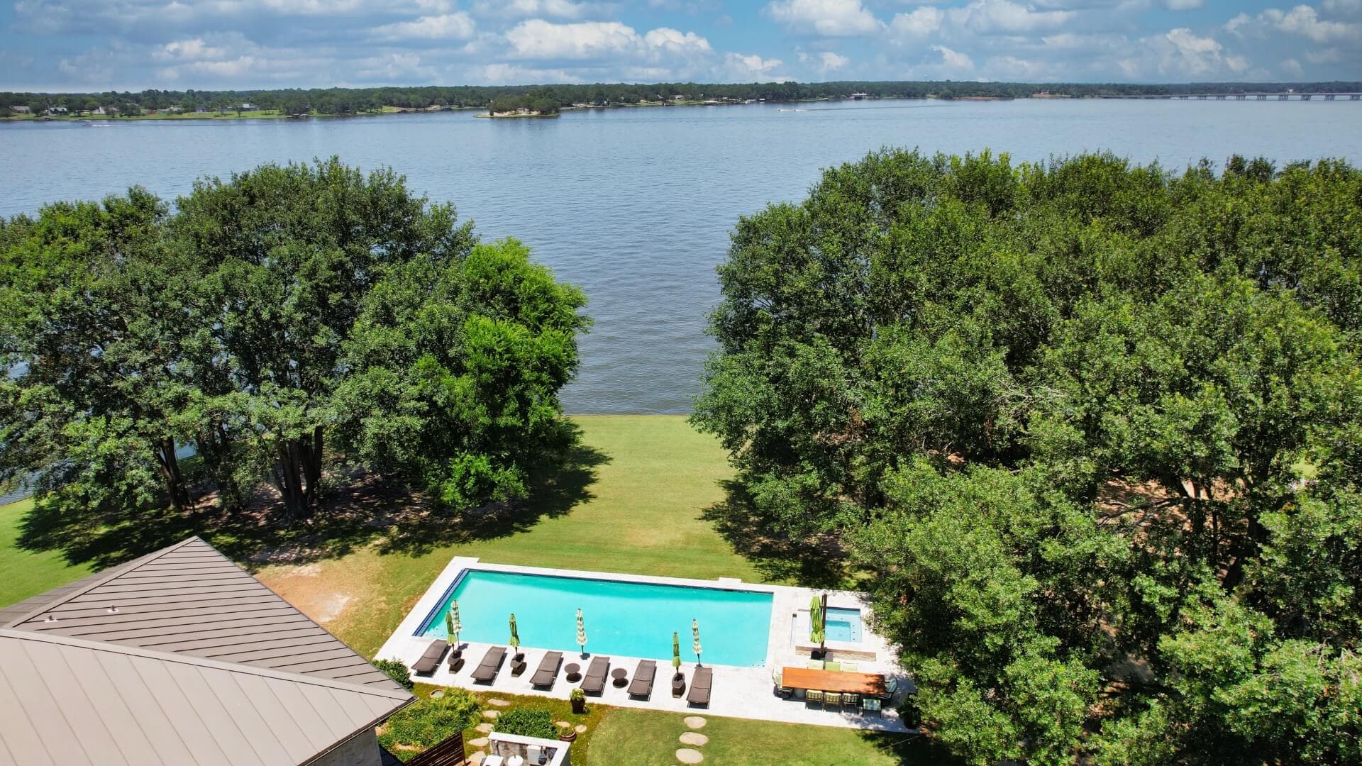 Aerial view of a lakeside property featuring a pool and lush greenery.