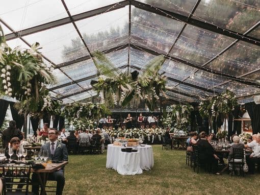A beautifully decorated tent with lush greenery and string lights, filled with guests enjoying a gathering.