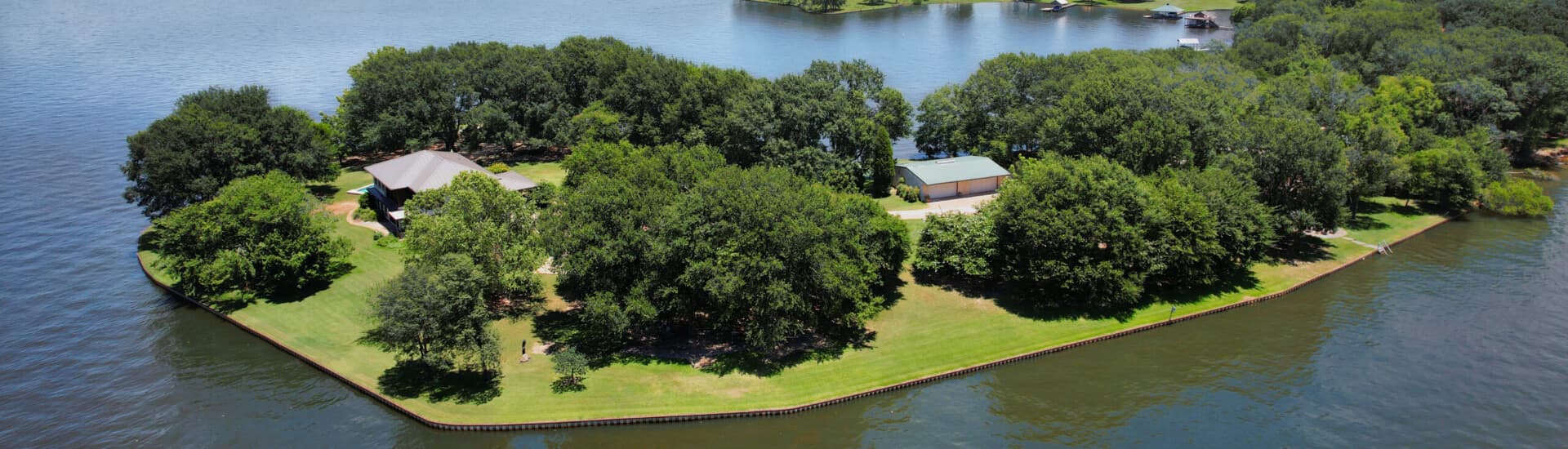 Aerial view of a lush, green island surrounded by water, featuring a few buildings and trees.