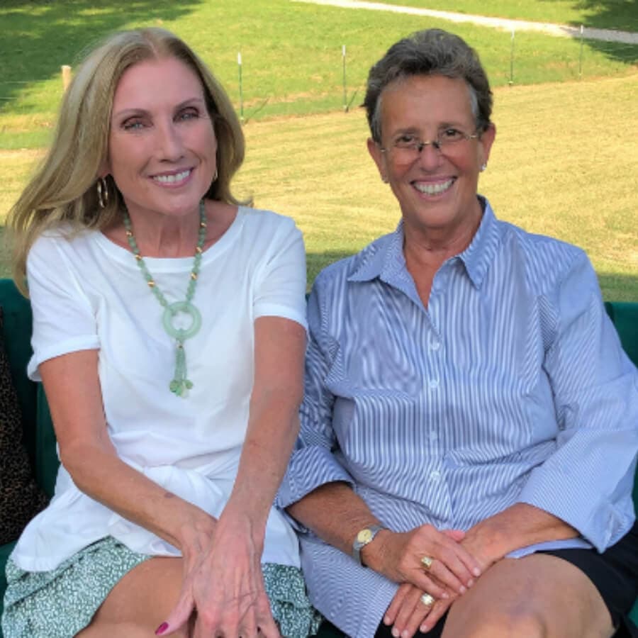 Two smiling women sitting together outdoors on a green couch.