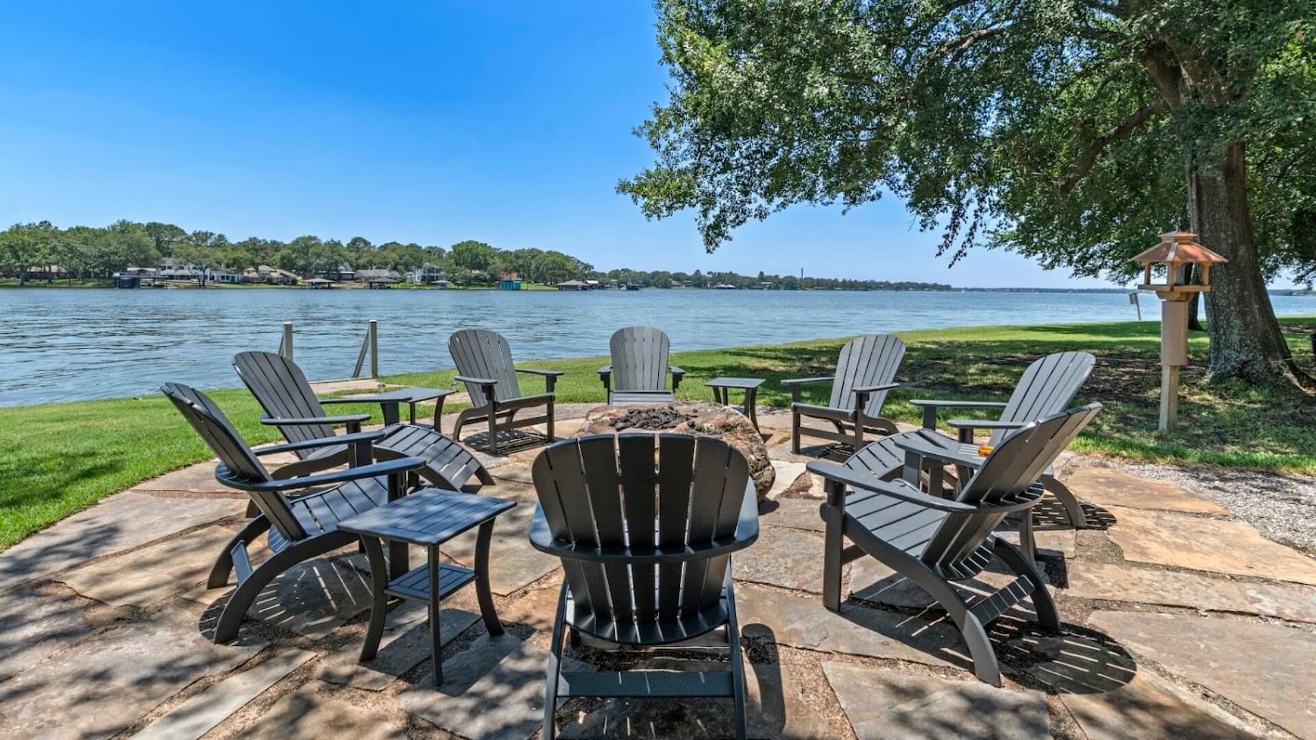 A circular seating area with black wooden chairs overlooks a calm lake on a sunny day.