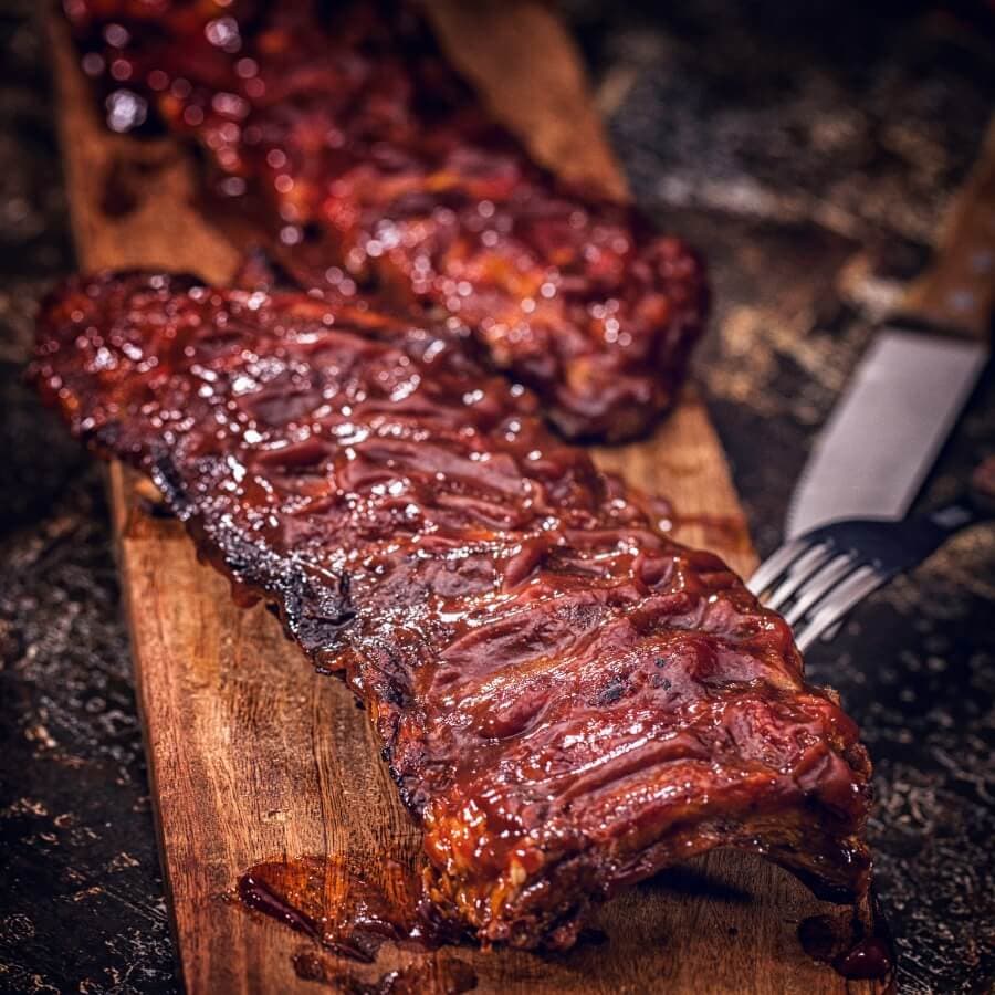 Barbecued ribs glazed with a sticky sauce, resting on a wooden cutting board.