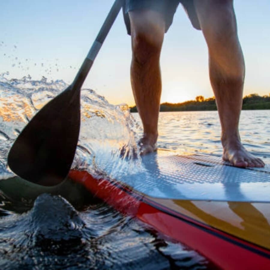 A person paddleboarding on a lake at sunset.