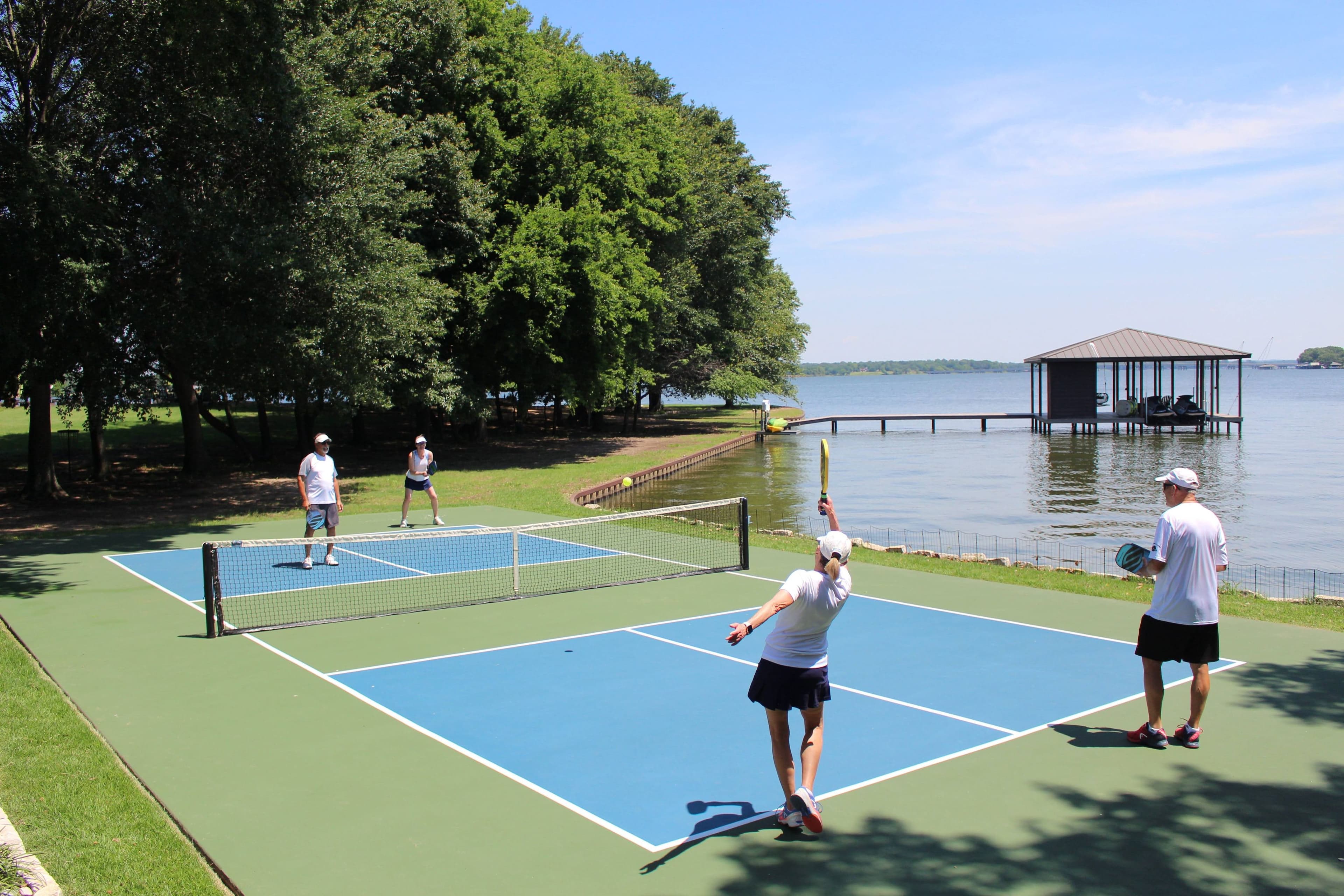 Four people playing pickleball on a court near a lake on a sunny day.